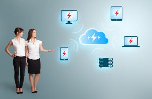Two women pointing to devices surrounded by a cloud to illustrate cloud computing.